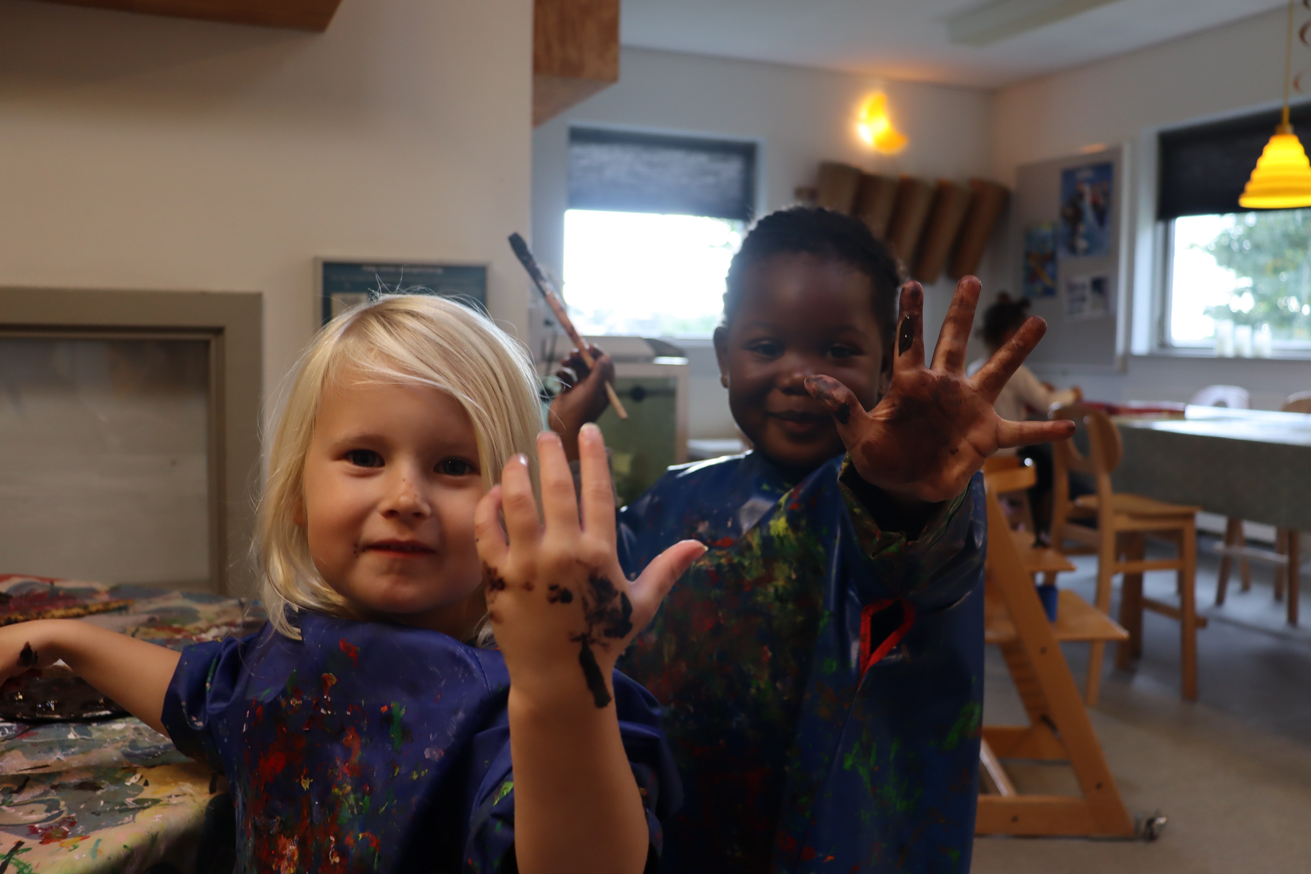 To børn viser deres malede hænder imens de maler på papmache