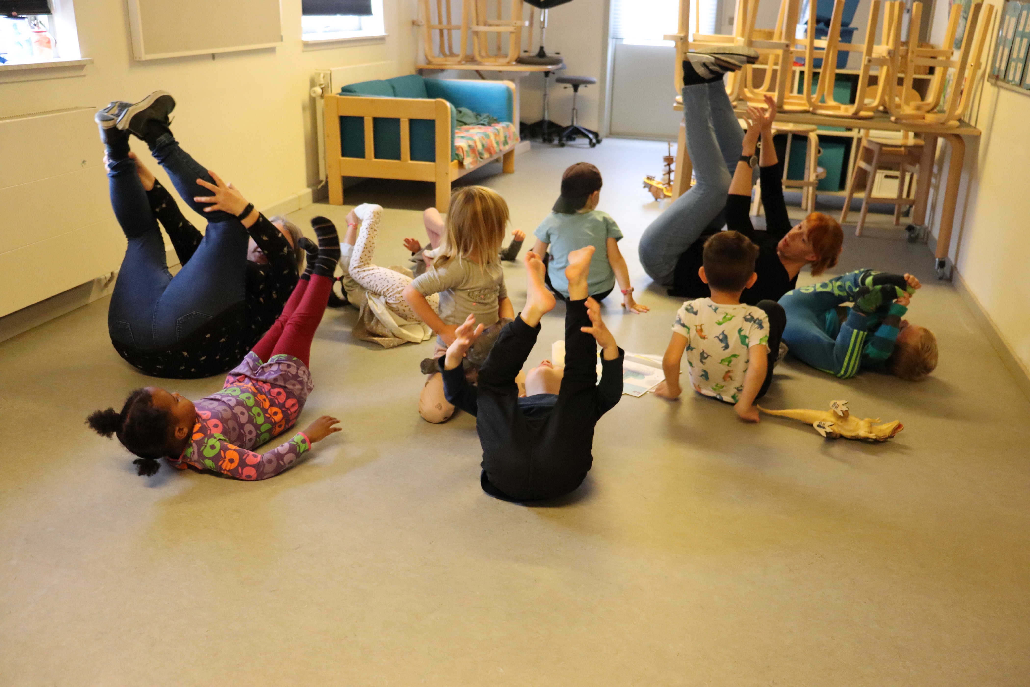 Børnehave gymnastik, hvor pædagoger og børn ligger på gulve og har benene oppe i luften