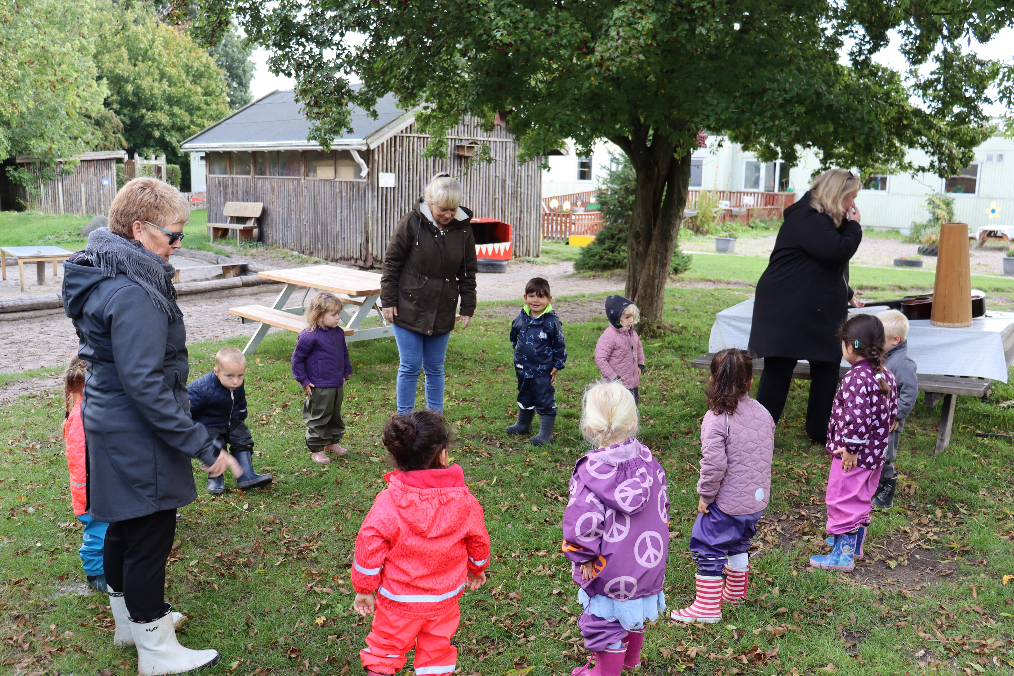 Pædagoger og børn samlet i cirkel udenfor, hvor de skal gøre klar til leg og sang